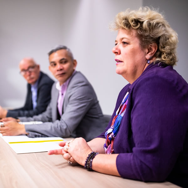 A women and two men sit at a desk